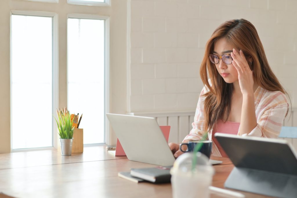 Girl student holding the glasses carefully while looking at laptop to prepare for graduate studies.