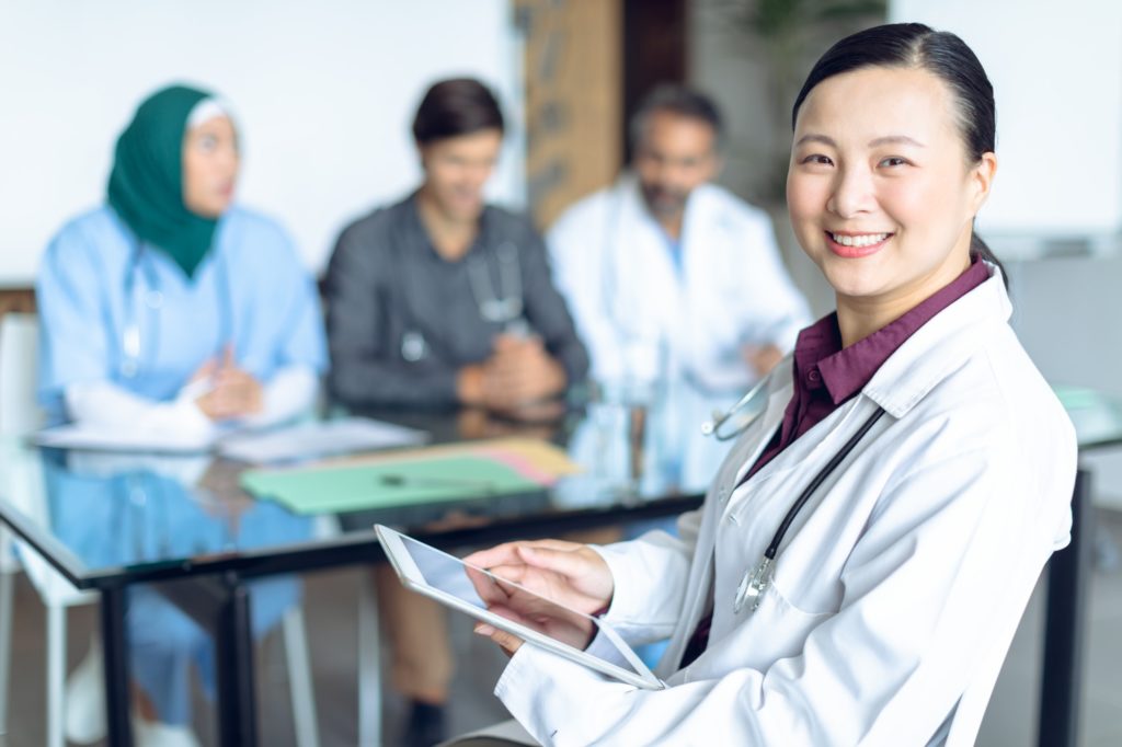 Happy Asian female doctor looking at camera while using digital tablet in the hospital.